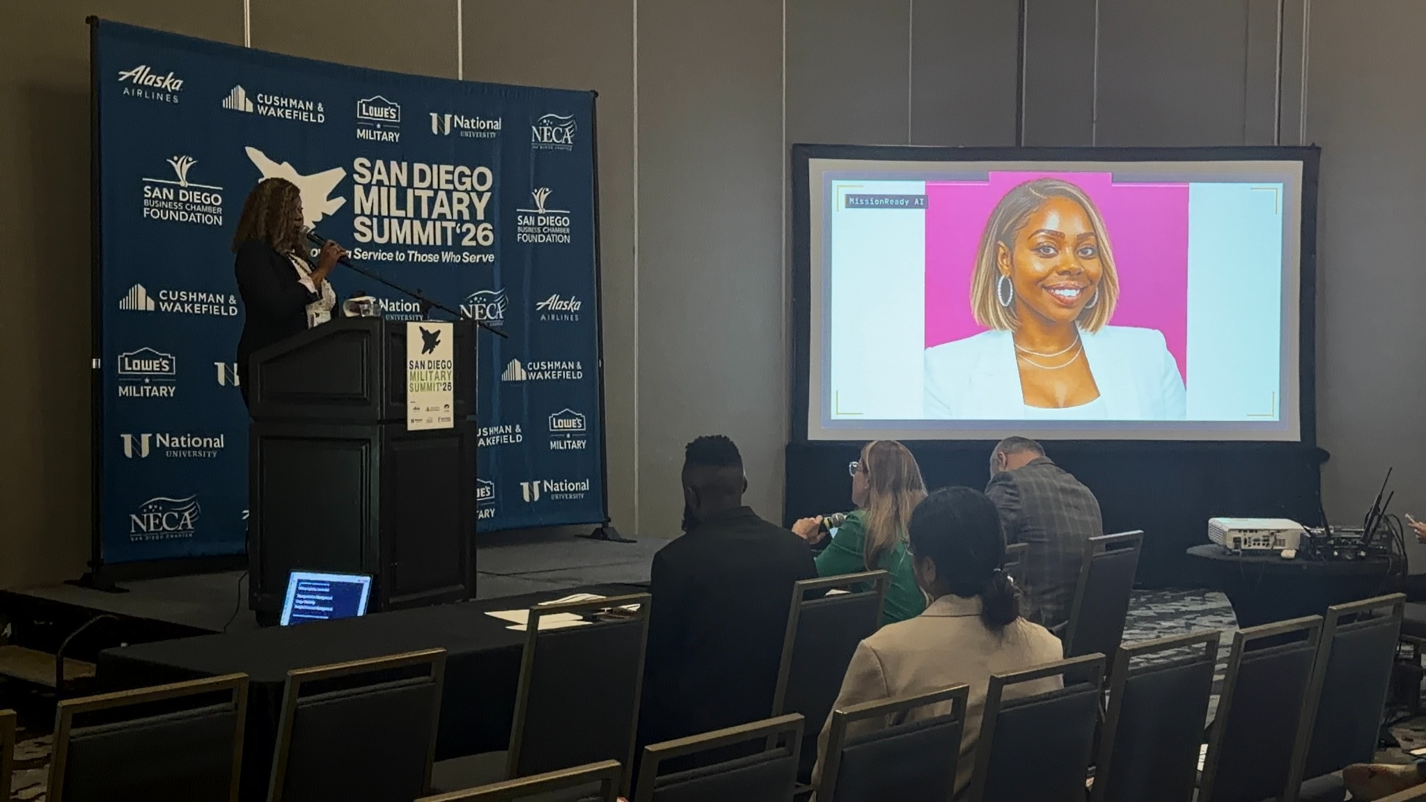 LaShea presenting MissionReady AI at a podium at the San Diego Military Summit, with her slide on screen